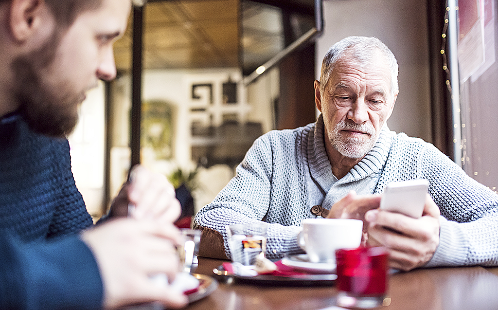 Äldre man med smartphone på kafé