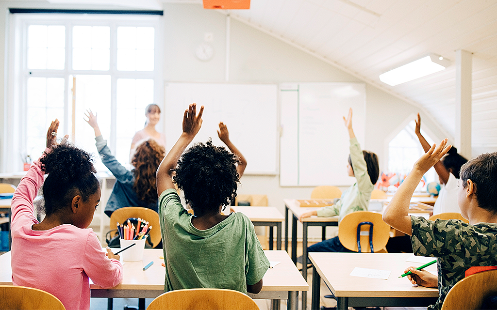 Mellanstadiebarn räcker upp handen i klassrum