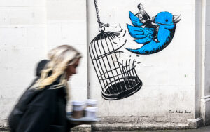 Kvinna i förgrunden promenerar förbi väggmålning med Twittermotiv